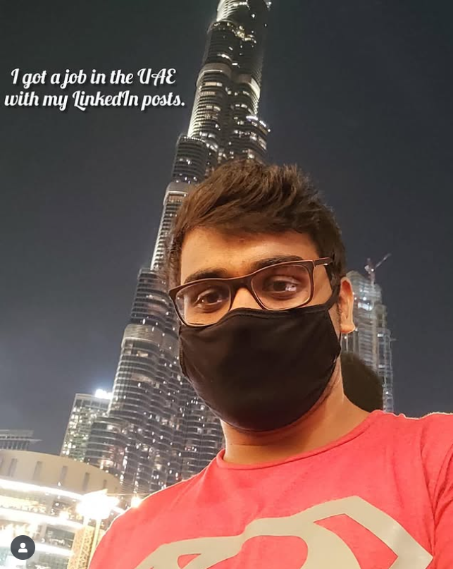 I’m taking a selfie at night in front of the Burj Khalifa, wearing glasses and a black face mask. The Dubai lights are behind me, and the image has text saying I got a job in the UAE through my LinkedIn posts.