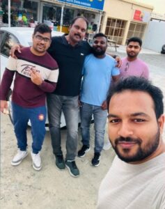 Group of friends taking a casual selfie during a long drive, standing near the road with relaxed smiles and a fun, easygoing vibe.